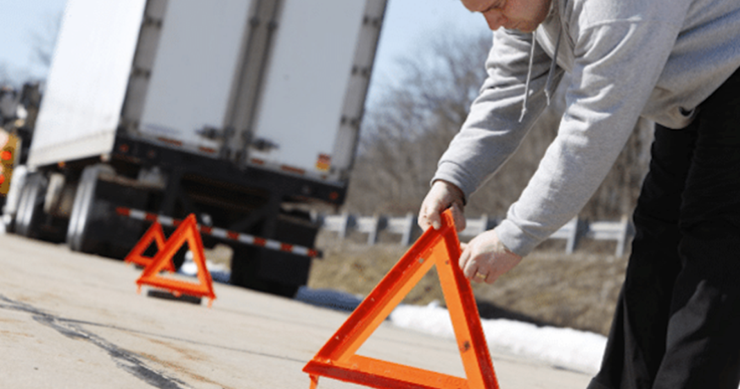 Camionneur en panne sur la route qui pose ses triangles de sécurité.