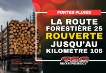 La route forestière 25 rouverte jusqu’au kilomètre 106 Camion forestier chargé de billots circulant sous la pluie, avec l’annonce de la réouverture de la route forestière 25 jusqu’au kilomètre 106.